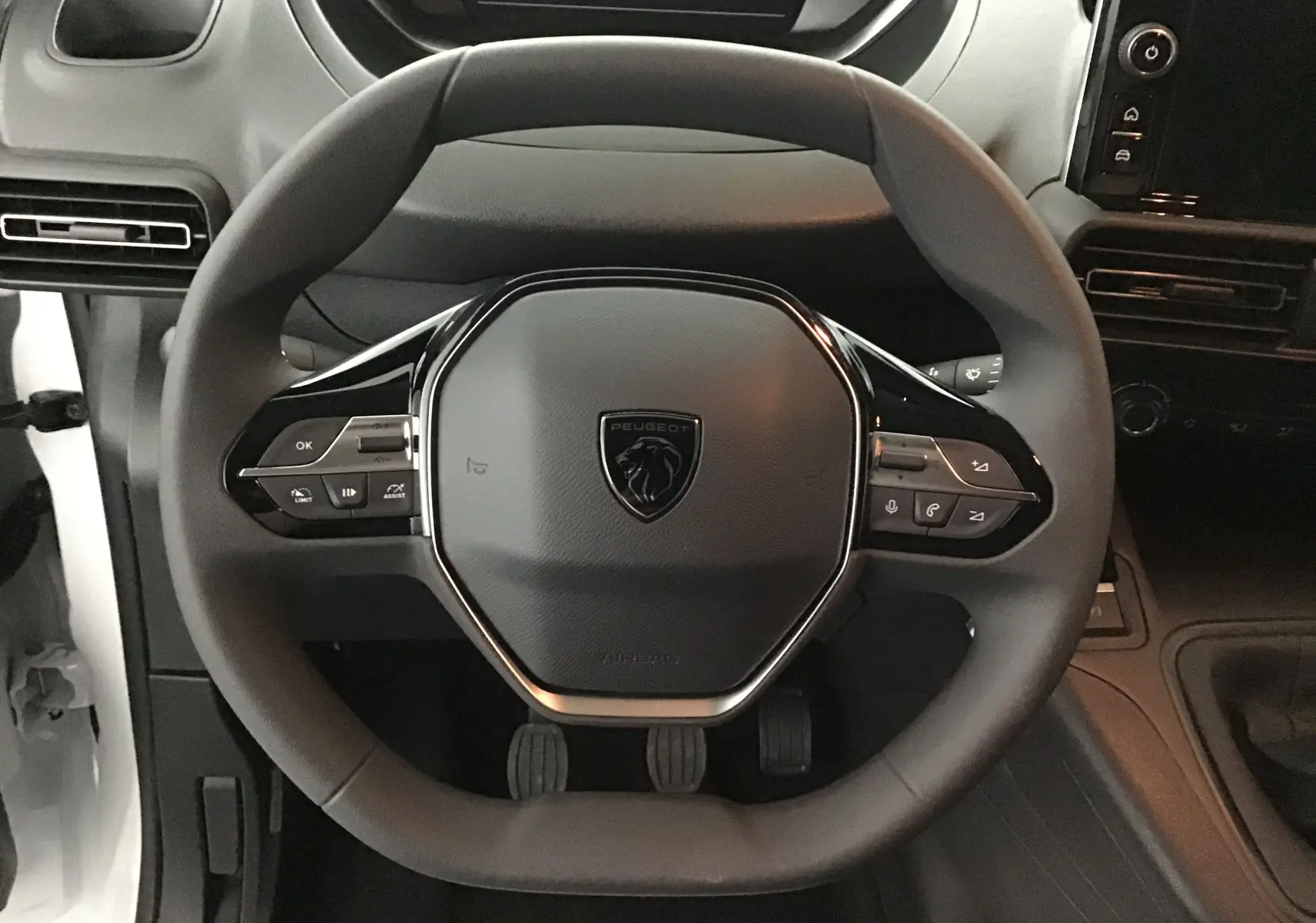 Vue rapprochée du volant noir du Peugeot Partner blanc, avec commandes intégrées et tableau de bord sombre en arrière-plan.