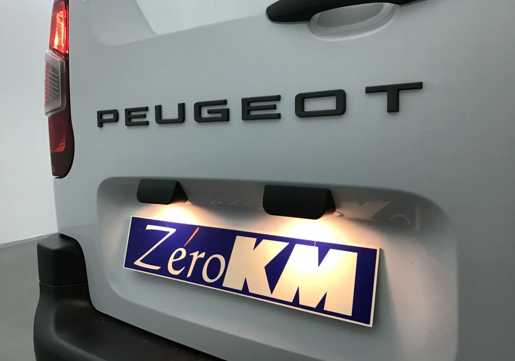 Gros plan arrière gauche du Peugeot Partner blanc montrant le logo et la plaque d'immatriculation éclairée "Zéro KM".