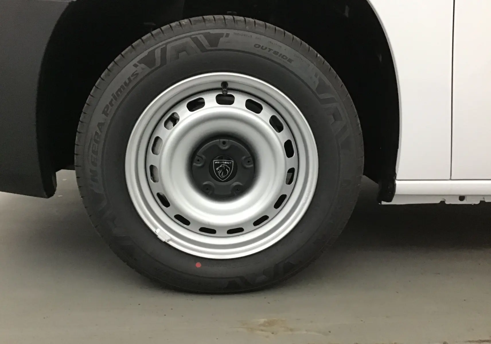 Gros plan sur la roue avant droite du Peugeot Partner blanc, avec jante acier et logo Peugeot au centre.