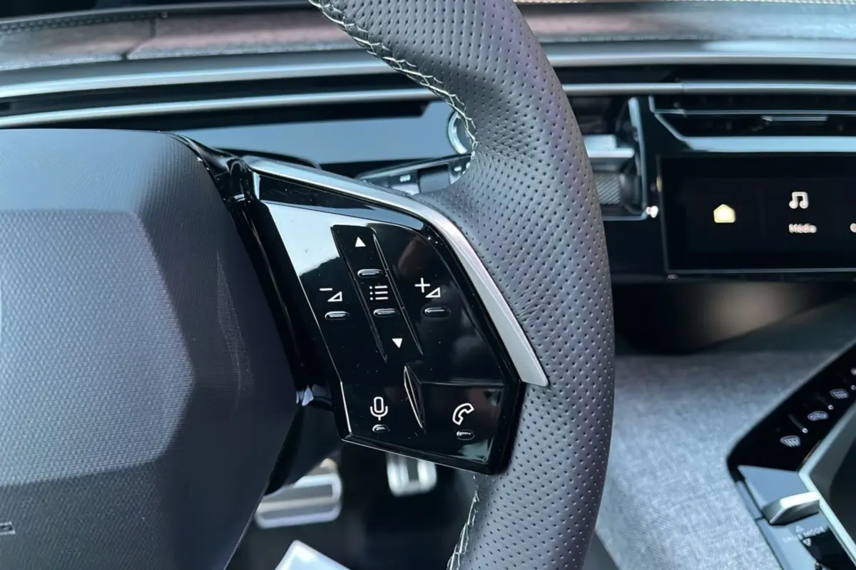 Gros plan sur la partie gauche du volant cuir perforé du Peugeot 5008 Hybrid 145 GT avec commandes multifonctions.