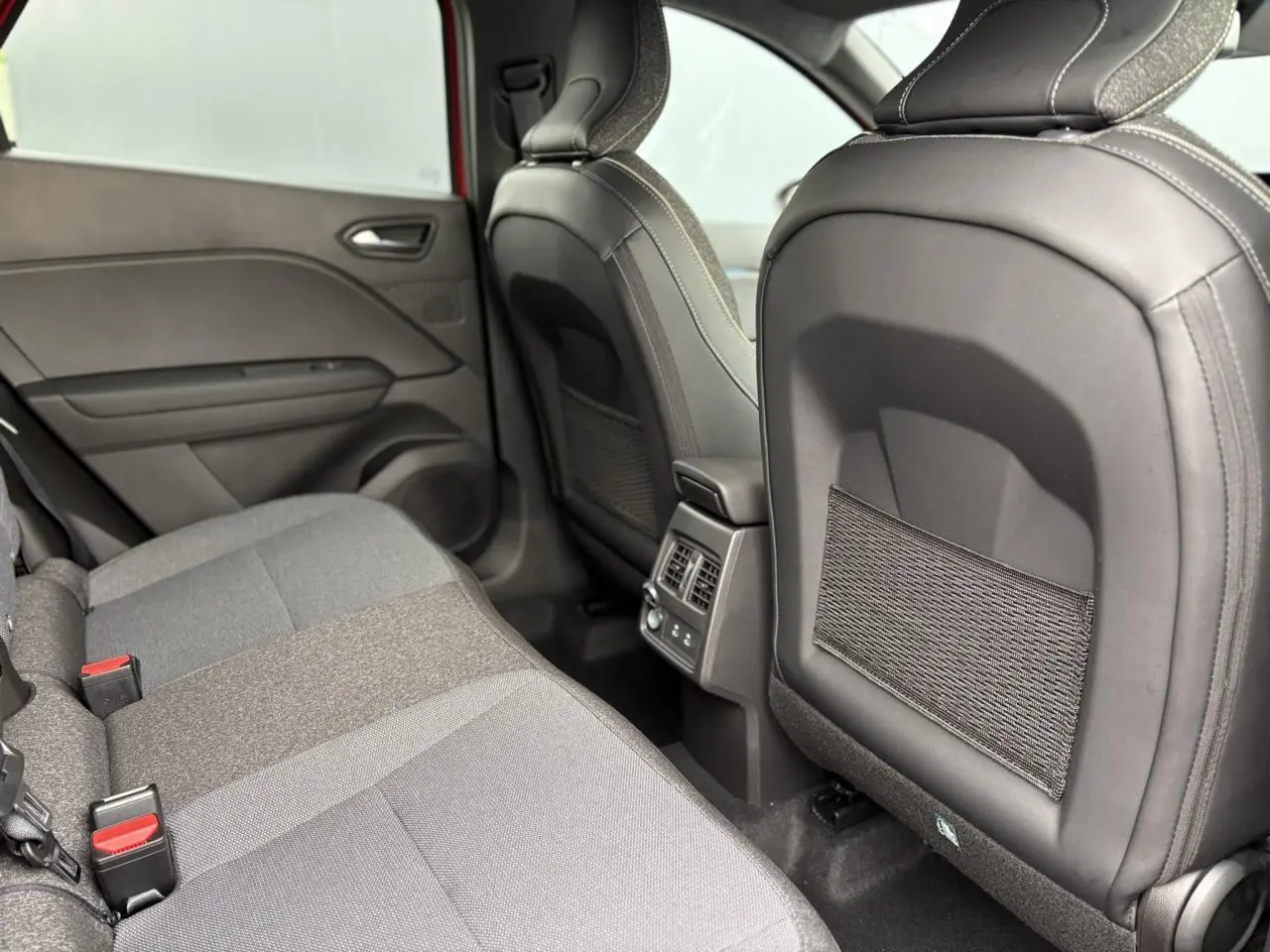 Vue intérieure arrière côté gauche du Renault Captur 2026, sièges tissu gris et dossiers avec filets de rangement.