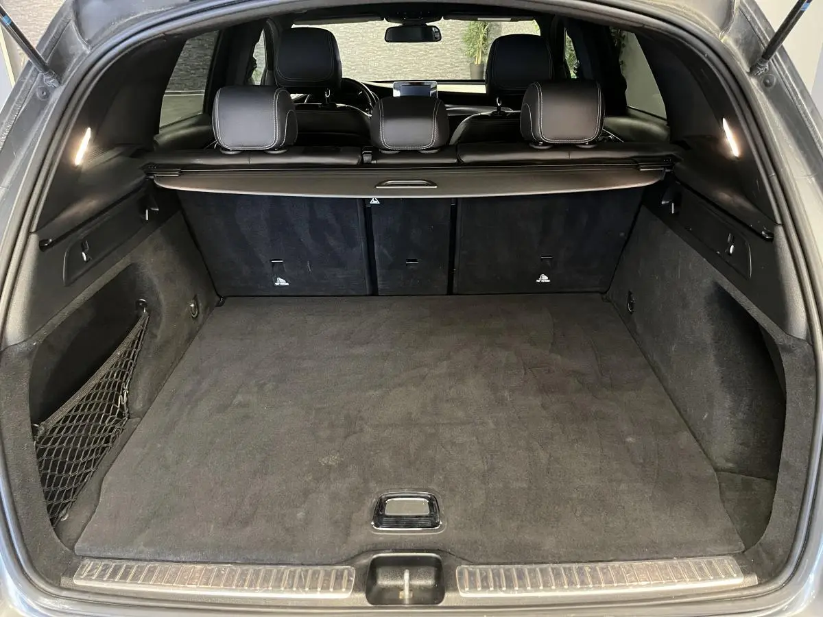 Coffre spacieux ouvert du Mercedes GLC 220 d Sportline gris, intérieur noir avec filet latéral et cache-bagages.