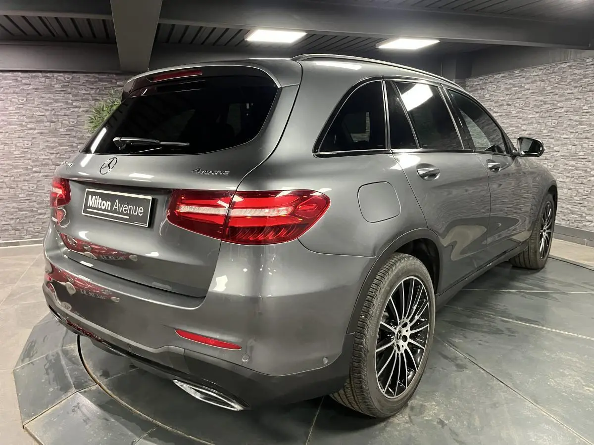 Vue 3/4 arrière droite d'un Mercedes GLC gris métallisé avec jantes AMG noires multibranches dans un garage.