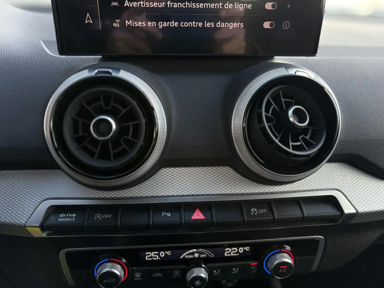 Détail du tableau de bord de l'Audi Q2 30 TDI S-Line 2025, montrant les aérateurs ronds et commandes de climatisation.