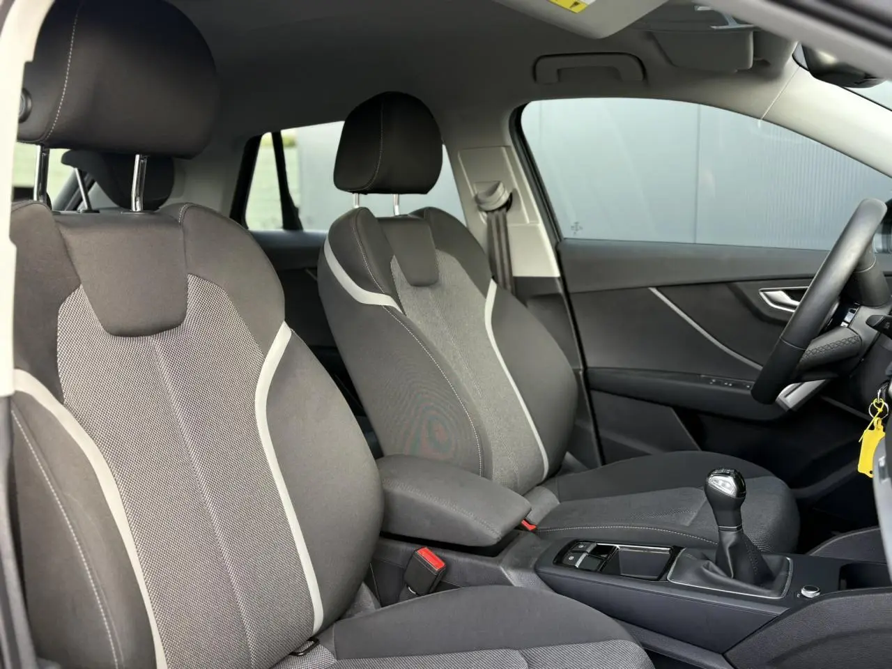 Vue intérieure côté droit montrant les sièges avant gris avec surpiqûres claires et la boîte manuelle d'un Audi Q2 30 TDI S-Line 2025.