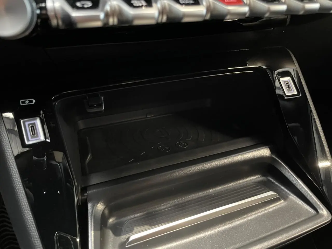 Gros plan sur la console centrale noire du Peugeot 2008 hybride 2026, avec zone de recharge sans fil et ports USB éclairés.