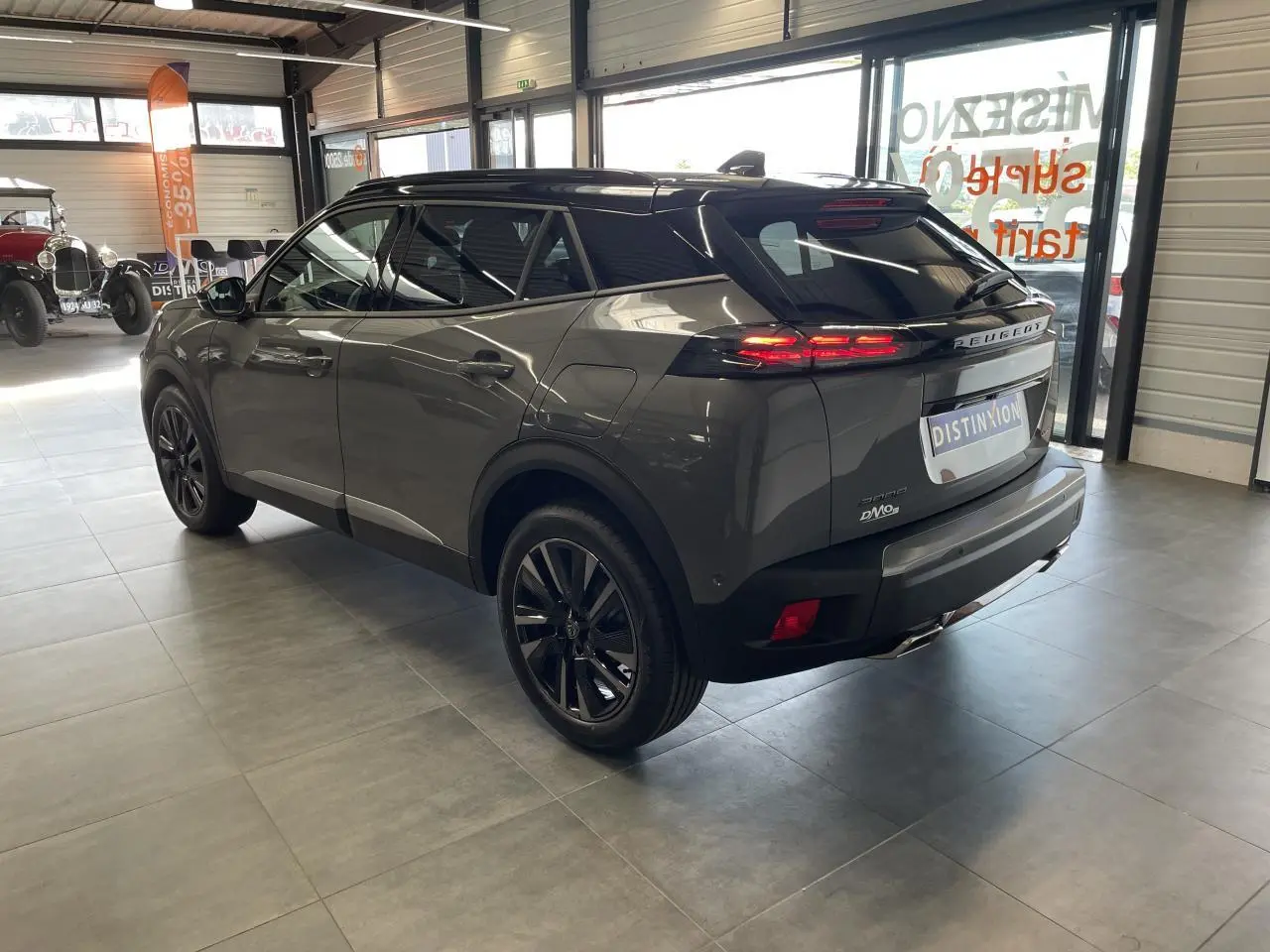 Vue 3/4 arrière droit d’un Peugeot 2008 gris hybride essence 2026 avec toit noir et jantes noires en showroom.