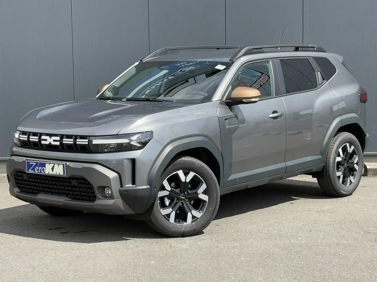 SUV Dacia Duster gris schiste en 3/4 avant droit avec coques de rétroviseurs brun cuivré et jantes alliage.