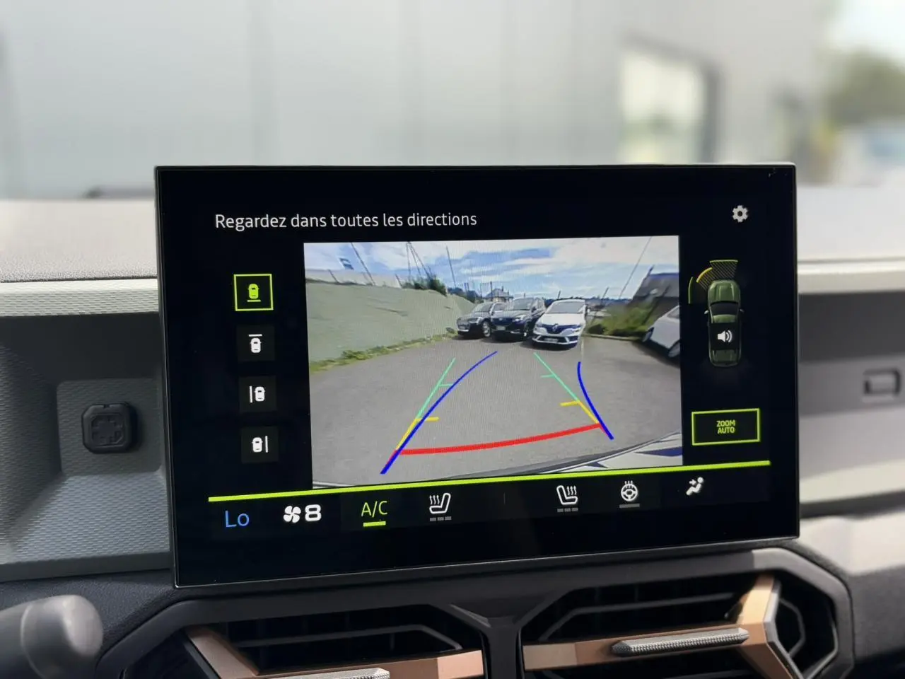 Écran tactile du Dacia Duster 2025 montrant la caméra de recul avec vue arrière sur un parking extérieur.
