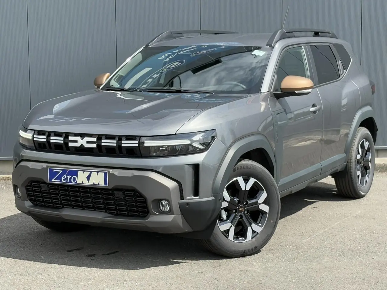 SUV Dacia Duster gris schiste en 3/4 avant droit avec coques de rétroviseur brun cuivré et jantes alliage noires.