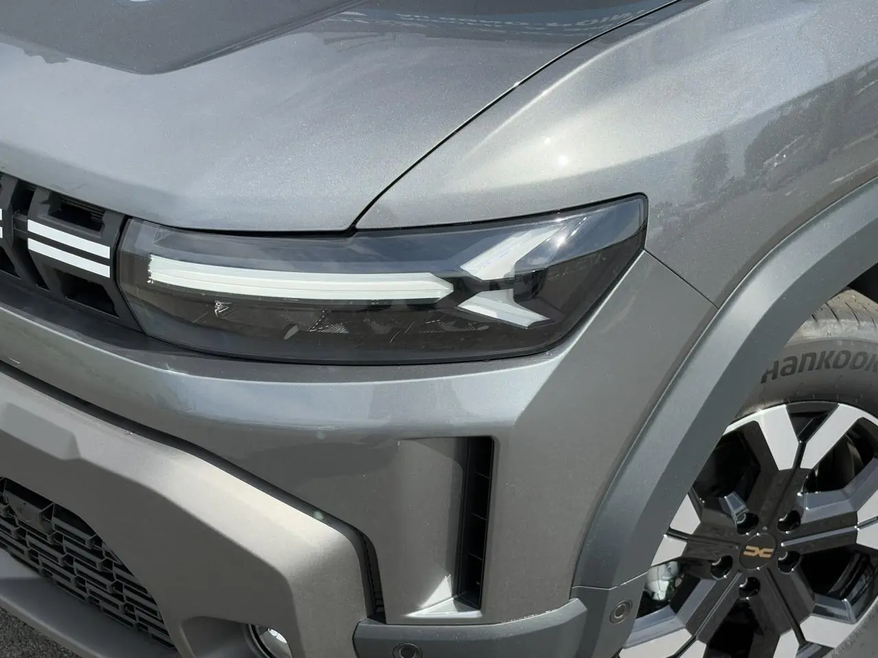 Gros plan sur l'avant droit du Dacia Duster gris schiste, mettant en valeur son phare LED et sa jante alliage noire et argentée.