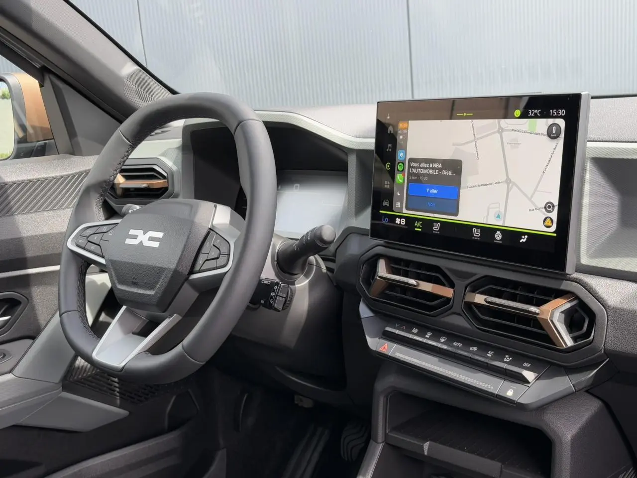 Vue intérieure du tableau de bord du Dacia Duster 2025 avec écran tactile GPS et volant multifonction noir.
