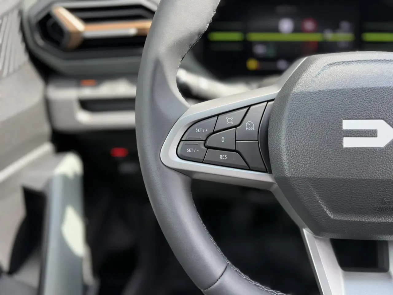 Gros plan sur le volant gris du Dacia Duster 2025 avec commandes intégrées et tableau de bord digital flou en arrière-plan
