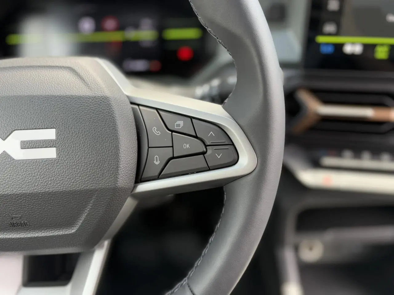 Gros plan sur le volant gris du Dacia Duster 2025 avec commandes vocales et écran digital flou en arrière-plan.