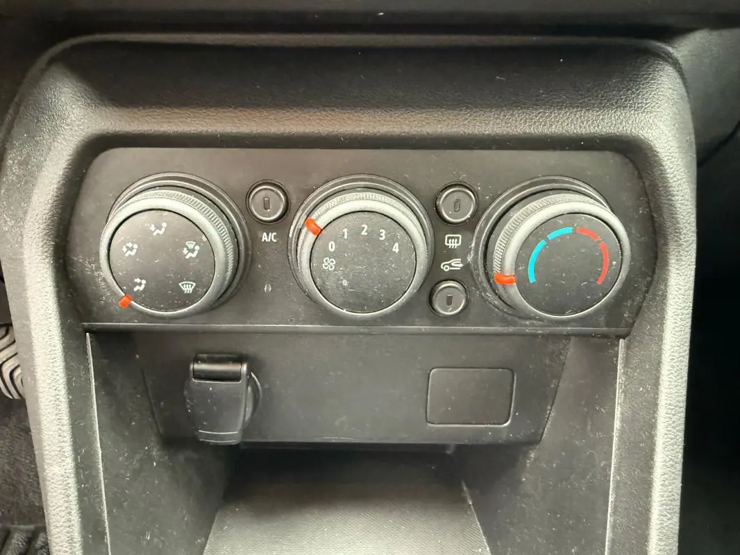 Panneau de commande de climatisation manuelle noir de la Dacia Sandero blanc, avec trois molettes et prise 12V visible.
