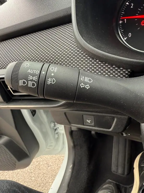 Gros plan sur la commande des phares et clignotants à gauche du volant dans une Dacia Sandero blanche 2021.