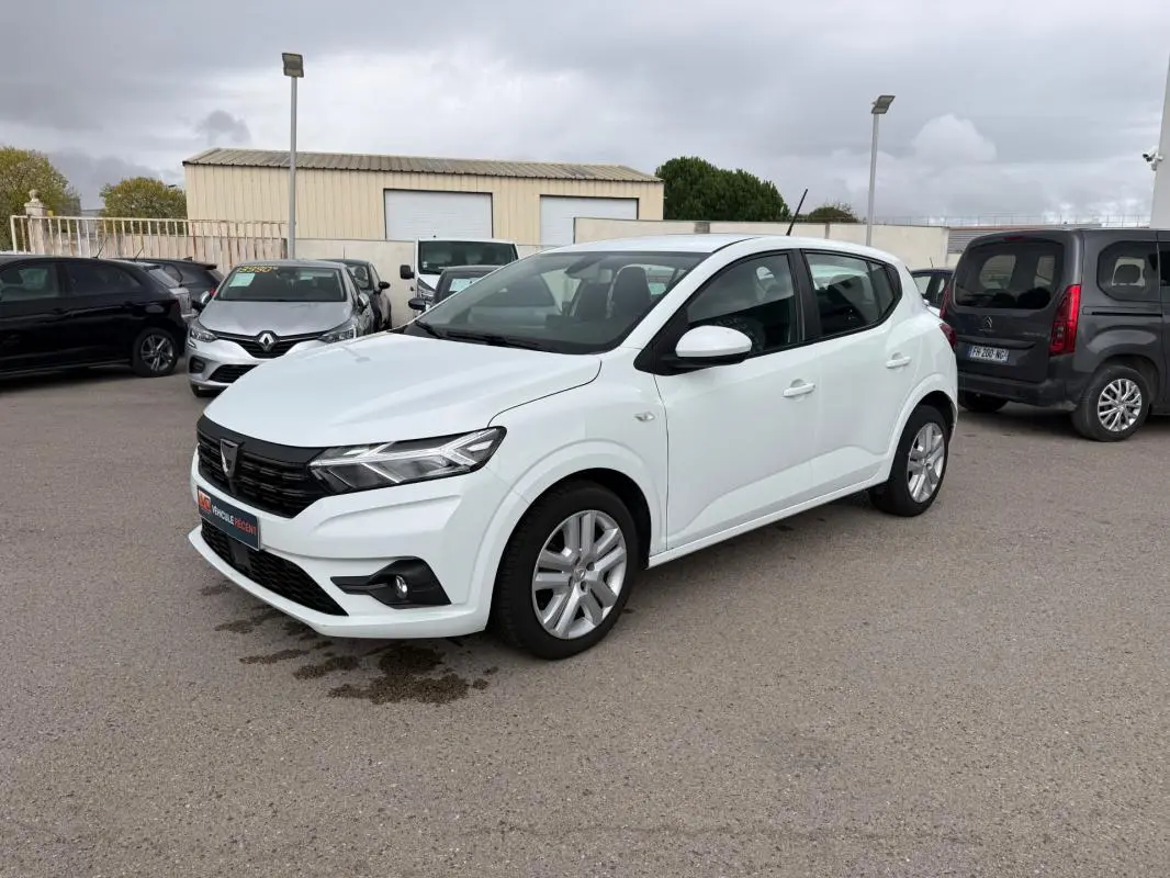 Vue 3/4 avant droite d'une Dacia Sandero blanche 2021 avec phares modernes et jantes alliage visibles.