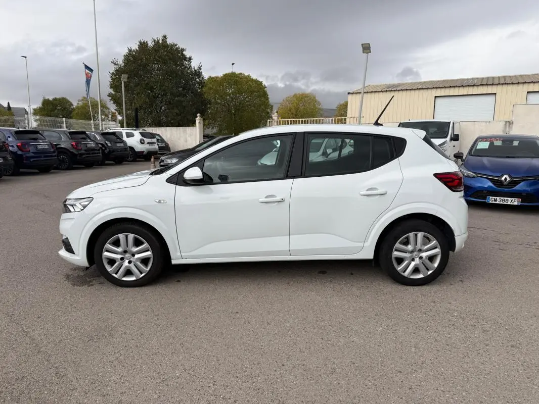 Profil côté gauche d'une Dacia Sandero blanche 2021, avec vitres surteintées et jantes alliage visibles.