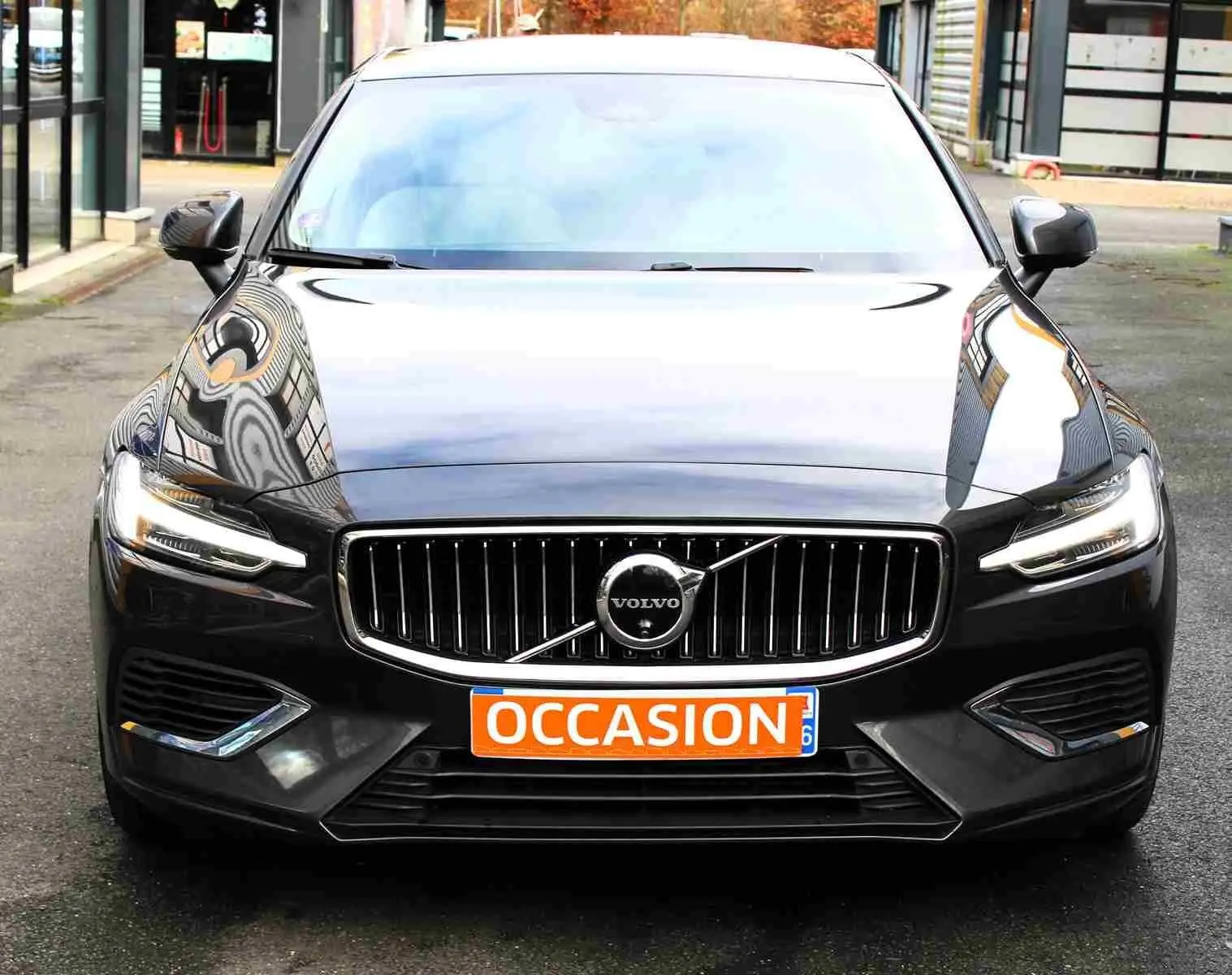 Vue frontale d'une Volvo S60 gris métal 2024 avec calandre chromée et phares LED allumés, plaque "OCCASION" visible.