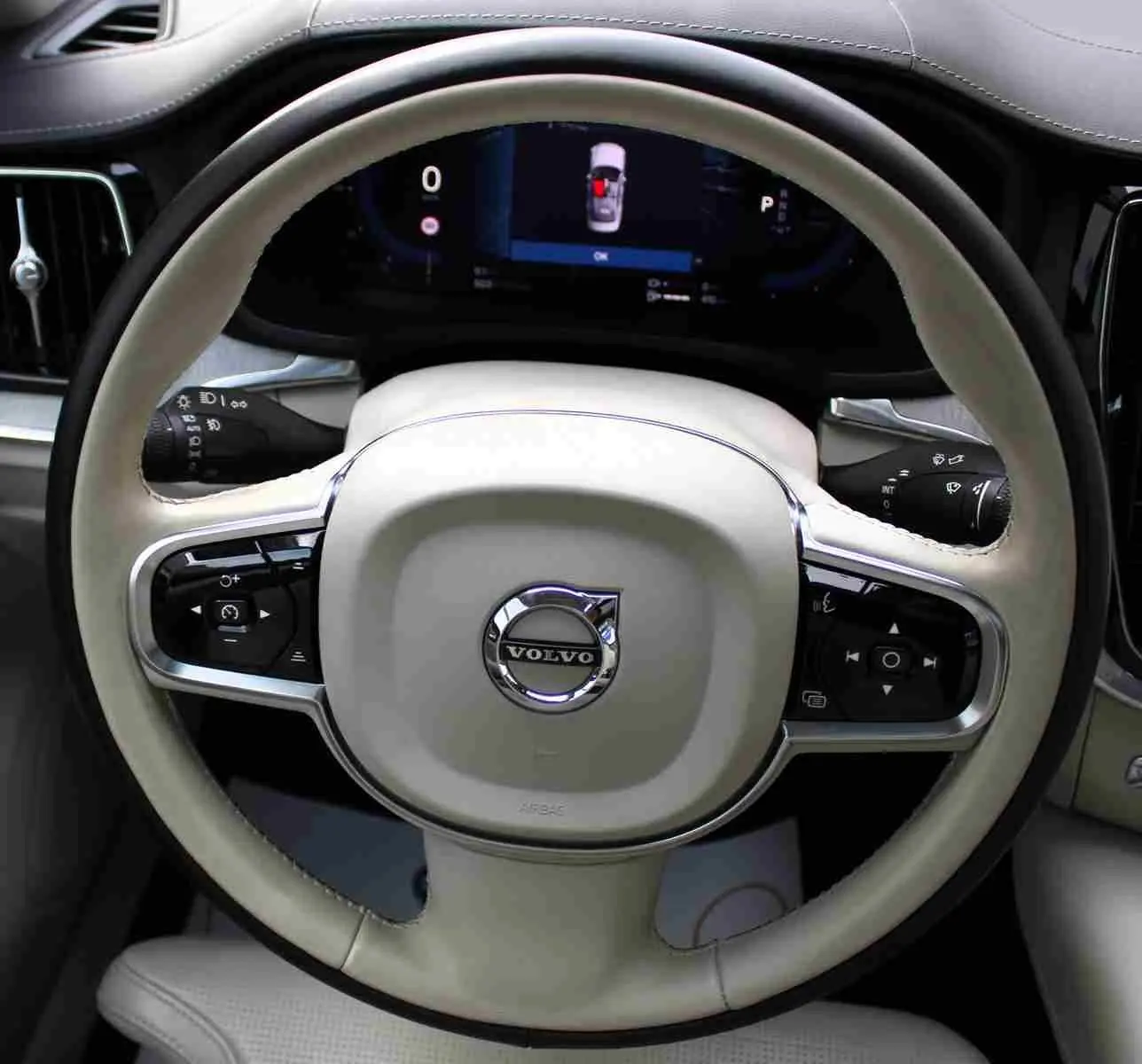 Gros plan sur le volant beige clair de la Volvo S60 2024 hybride rechargeable avec commandes intégrées et tableau de bord numérique.