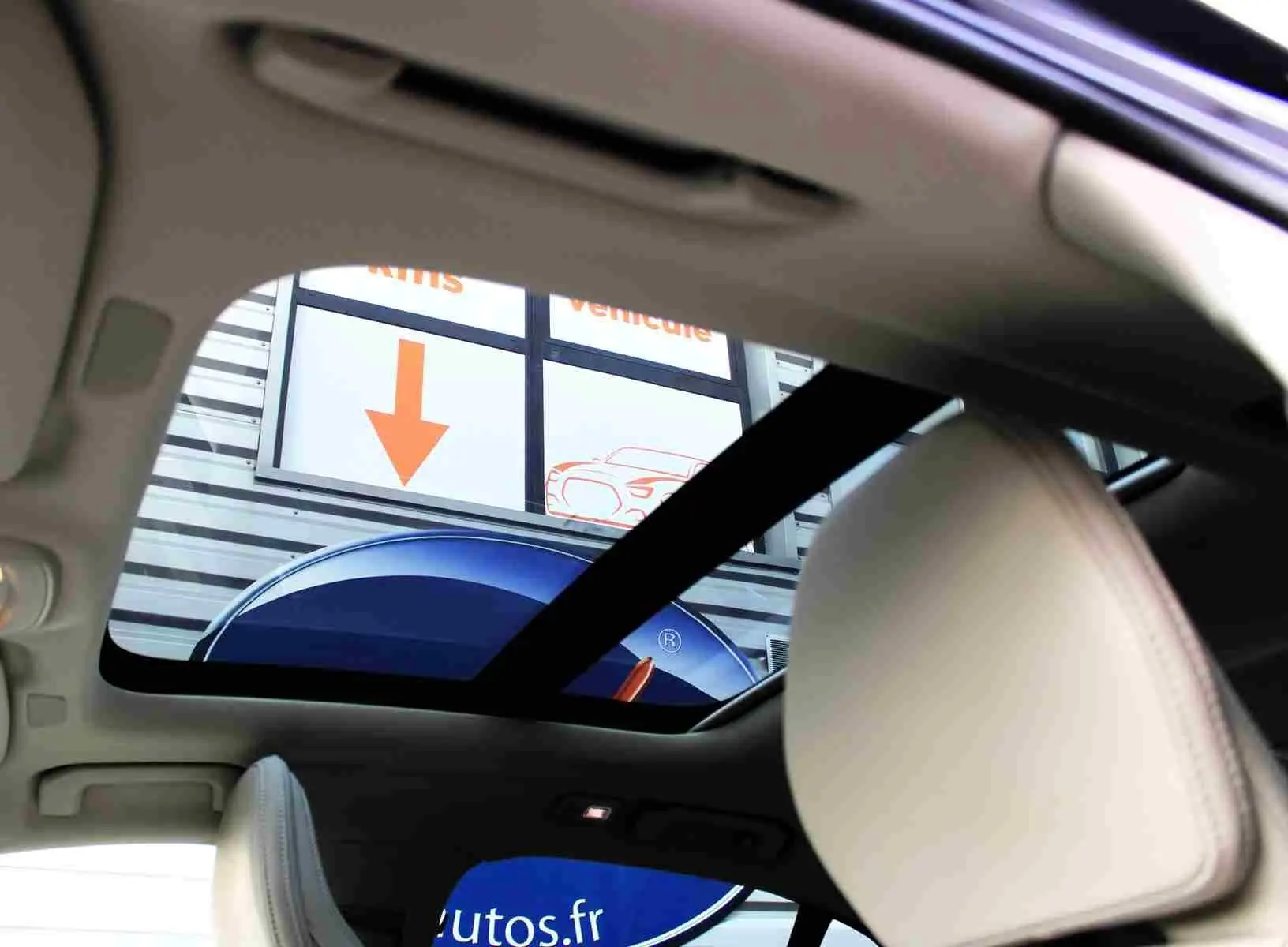 Vue intérieure du toit ouvrant panoramique d'une Volvo S60 gris métal 2024, avec appuie-tête beige visible.