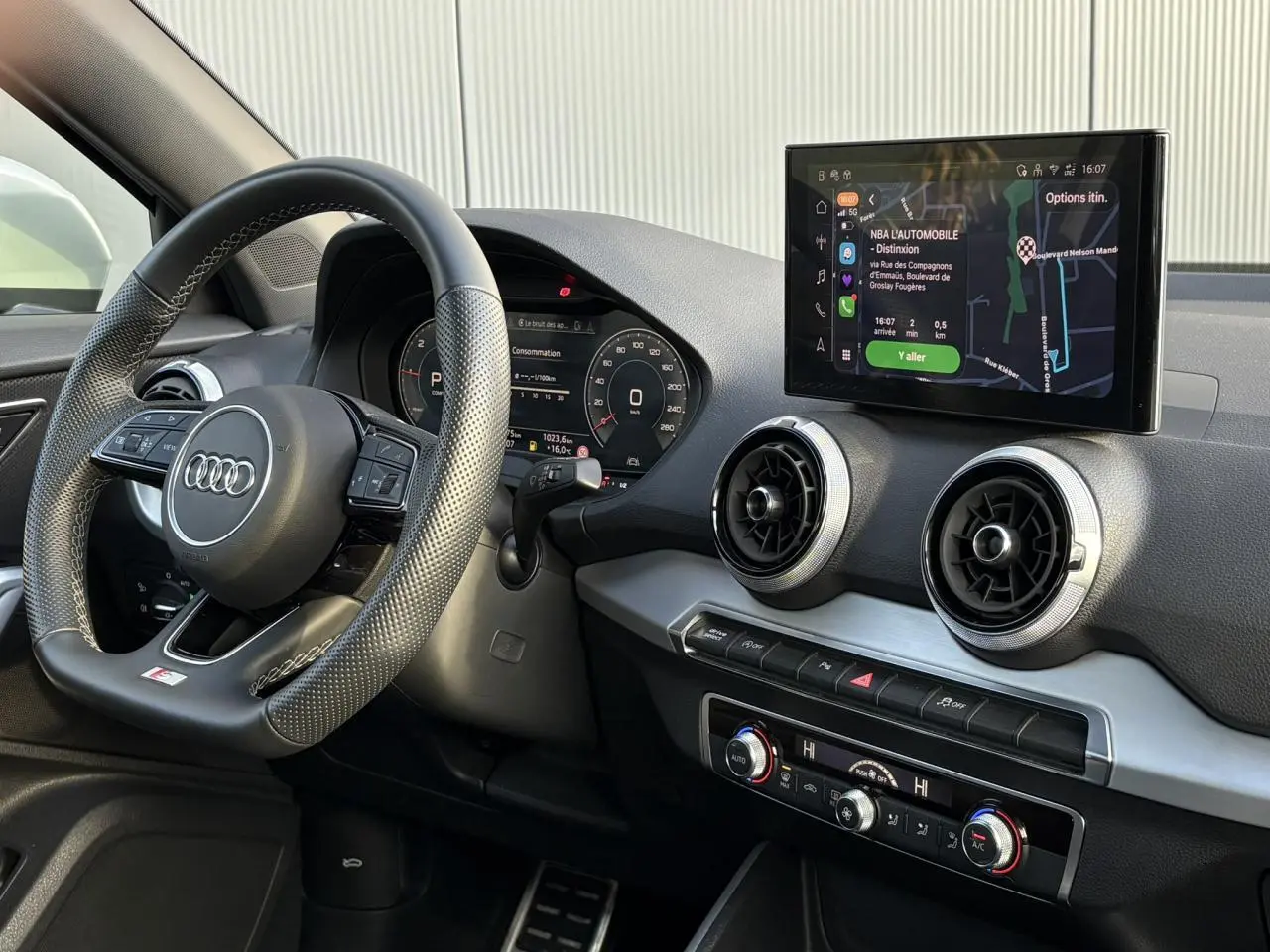 Vue intérieure côté conducteur de l'Audi Q2 35 TDI S-Line 2025, volant cuir et écran tactile MMI avec navigation.