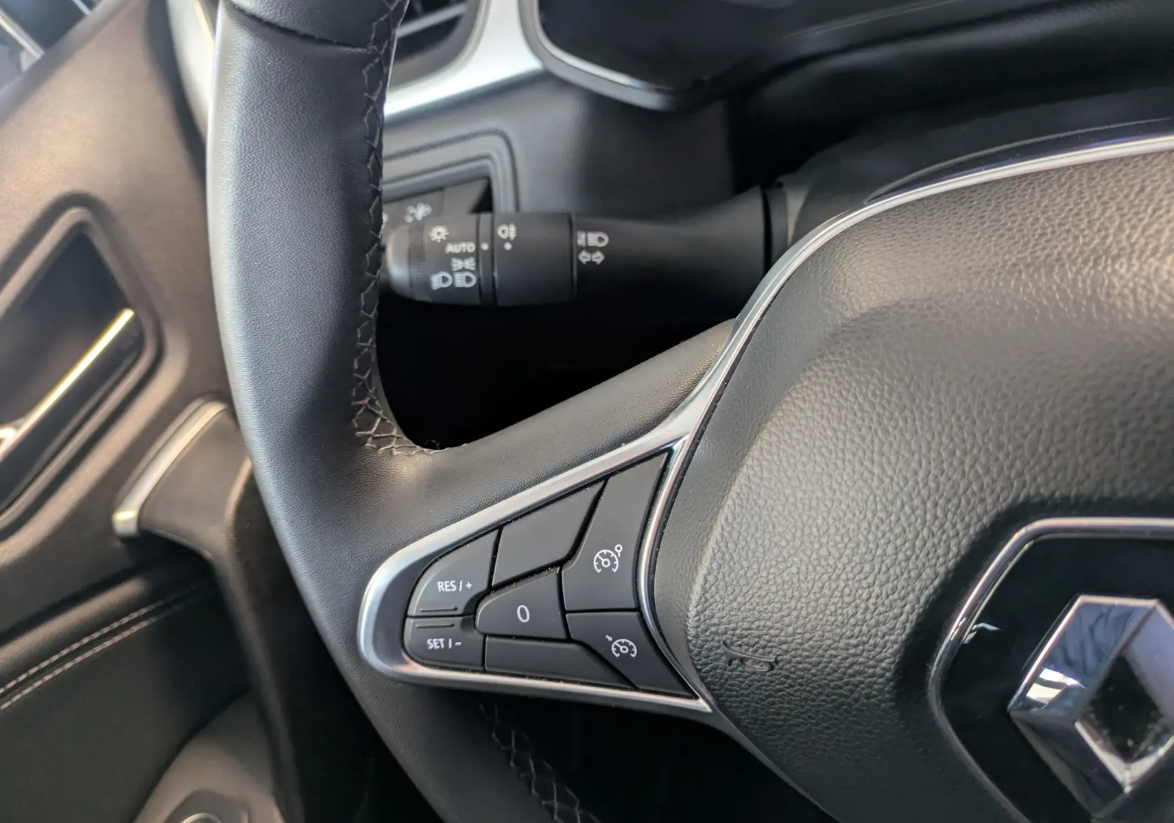 Gros plan sur le volant cuir noir du Renault Captur II Techno 2023 avec commandes de régulateur de vitesse intégrées.