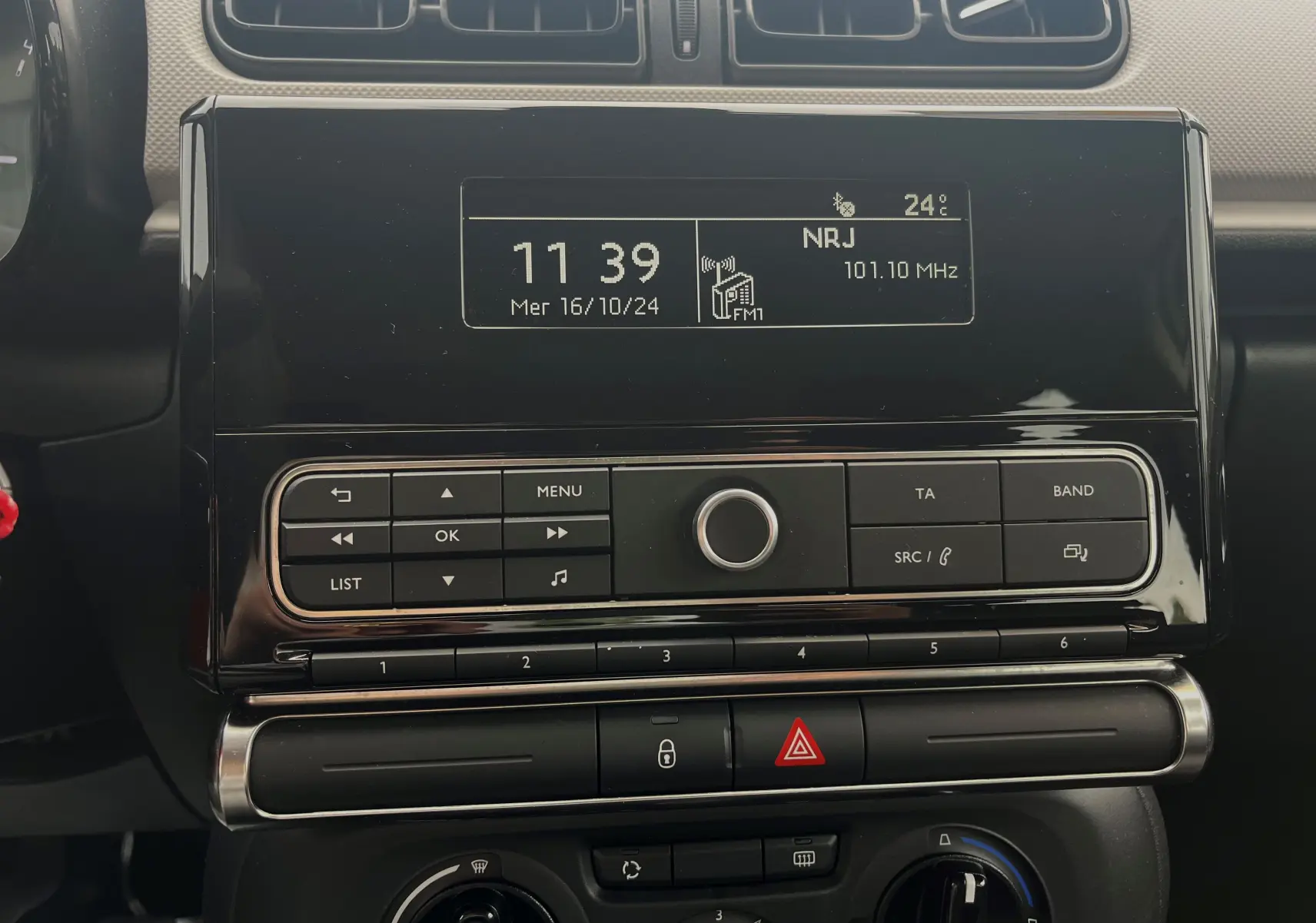 Détail de la console centrale noire de la Citroën C3 blanche 2017, affichant l'horloge et la radio NRJ FM.