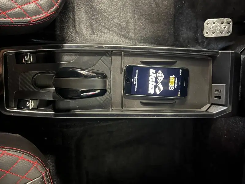 Vue plongeante sur la console centrale noire du Ligier JS50 gris 2025 avec levier de vitesses manuel et smartphone posé.