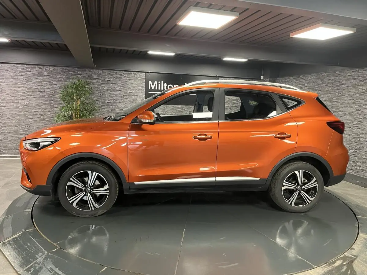 Profil côté gauche du SUV MG ZS 2022 orange métallisé avec jantes alliage et barres de toit visibles.