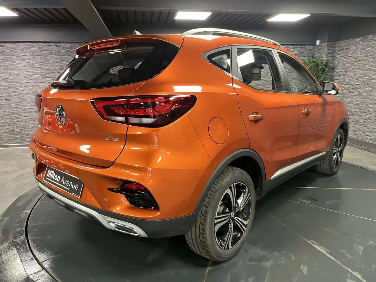 Vue 3/4 arrière droite d'un MG ZS orange métallisé 2022 avec jantes alliage et feux arrière LED dans un showroom.