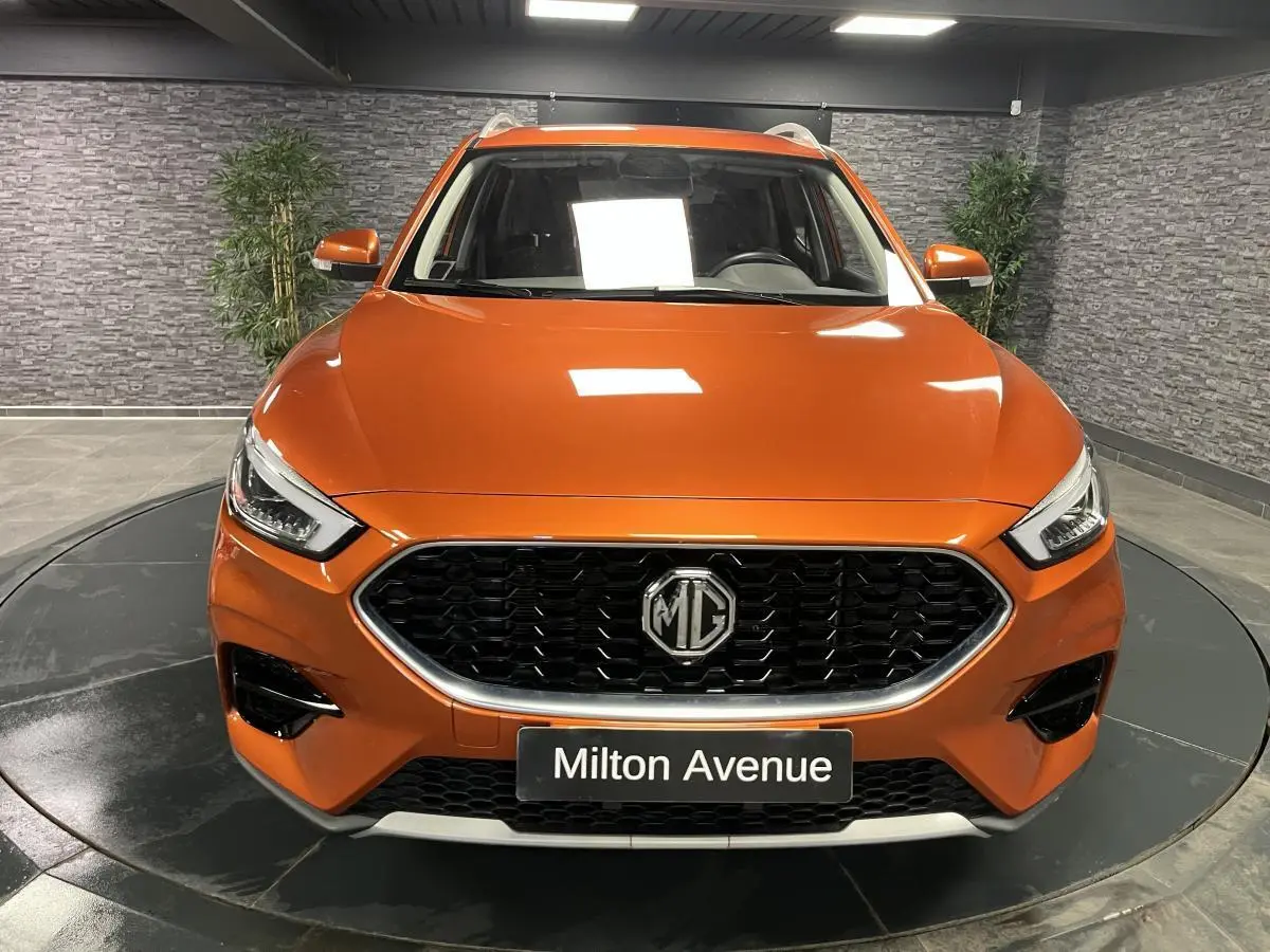 Vue frontale d'un MG ZS orange métallisé avec calandre noire et logo MG bien visible, en intérieur showroom.