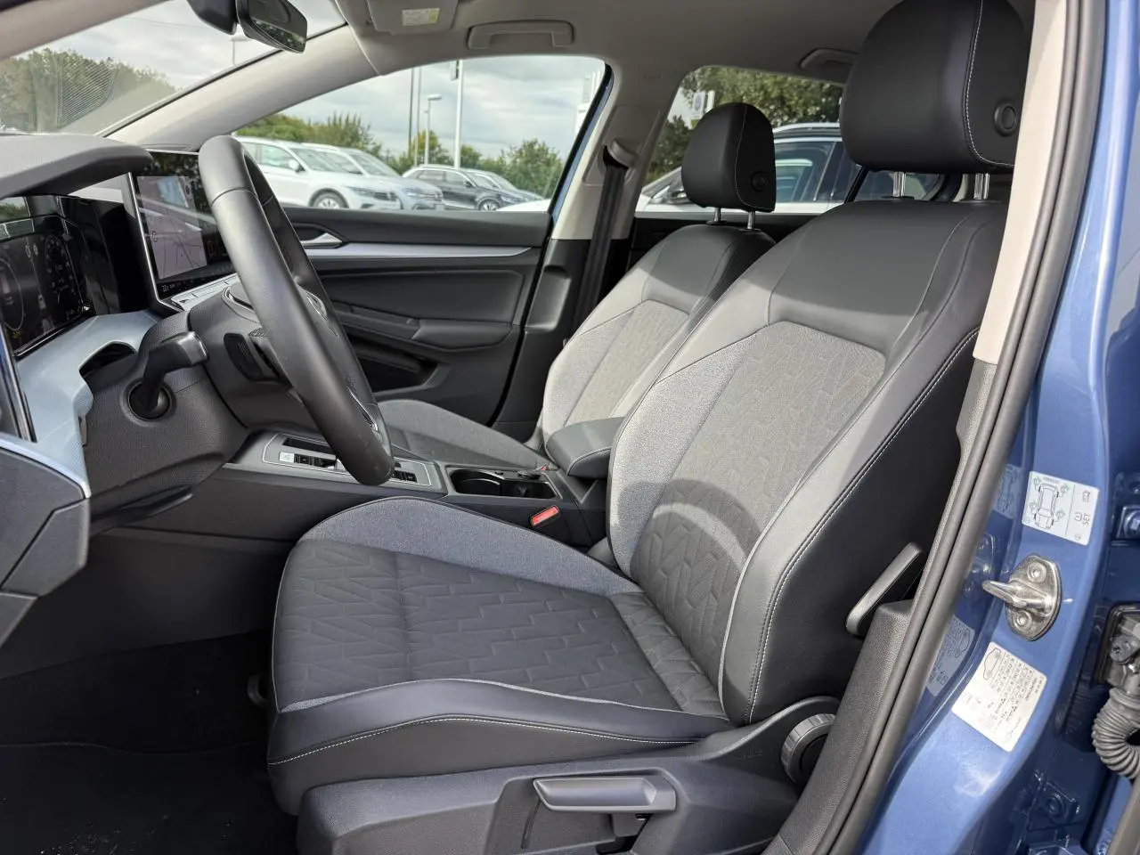 Vue intérieure côté conducteur de la Volkswagen Golf 2024 bleu anémone, sièges tissu et cuir noir avec tableau de bord digital.