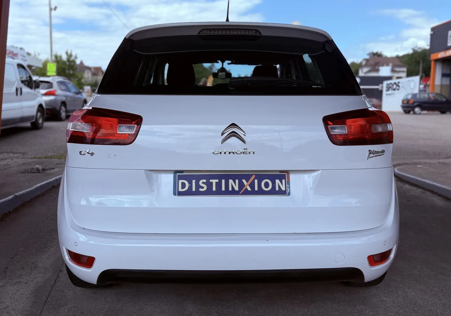 Vue arrière d'une Citroën C4 Picasso blanche de 2014 avec feux rouges et plaque d'immatriculation Distinxion.