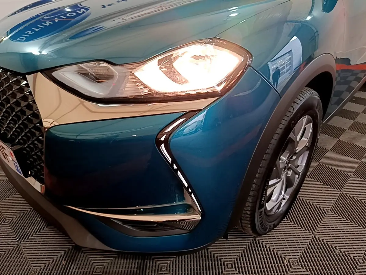 Gros plan sur l'avant droit bleu du DS3 Crossback 2020 avec phare allumé et calandre distinctive en losange.