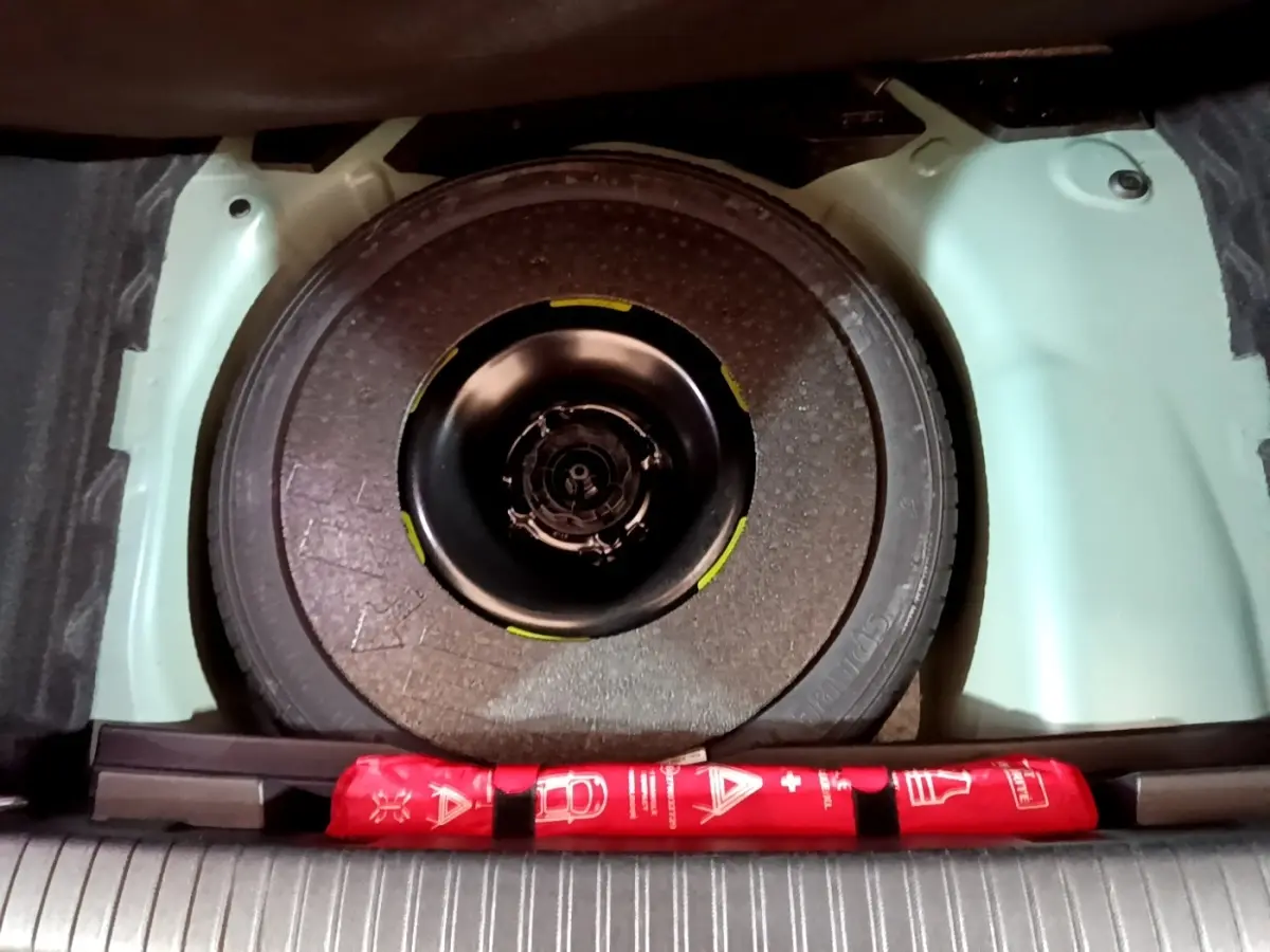 Vue plongeante sur la roue galette noire dans le coffre bleu clair du DS3 Crossback avec trousse de secours rouge.