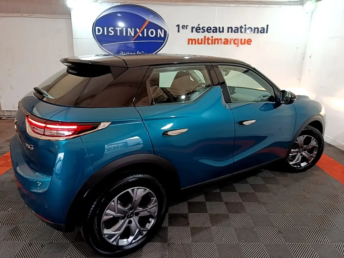 Vue 3/4 arrière droite d'un DS3 Crossback bleu avec toit noir et feux arrière LED dans un showroom.