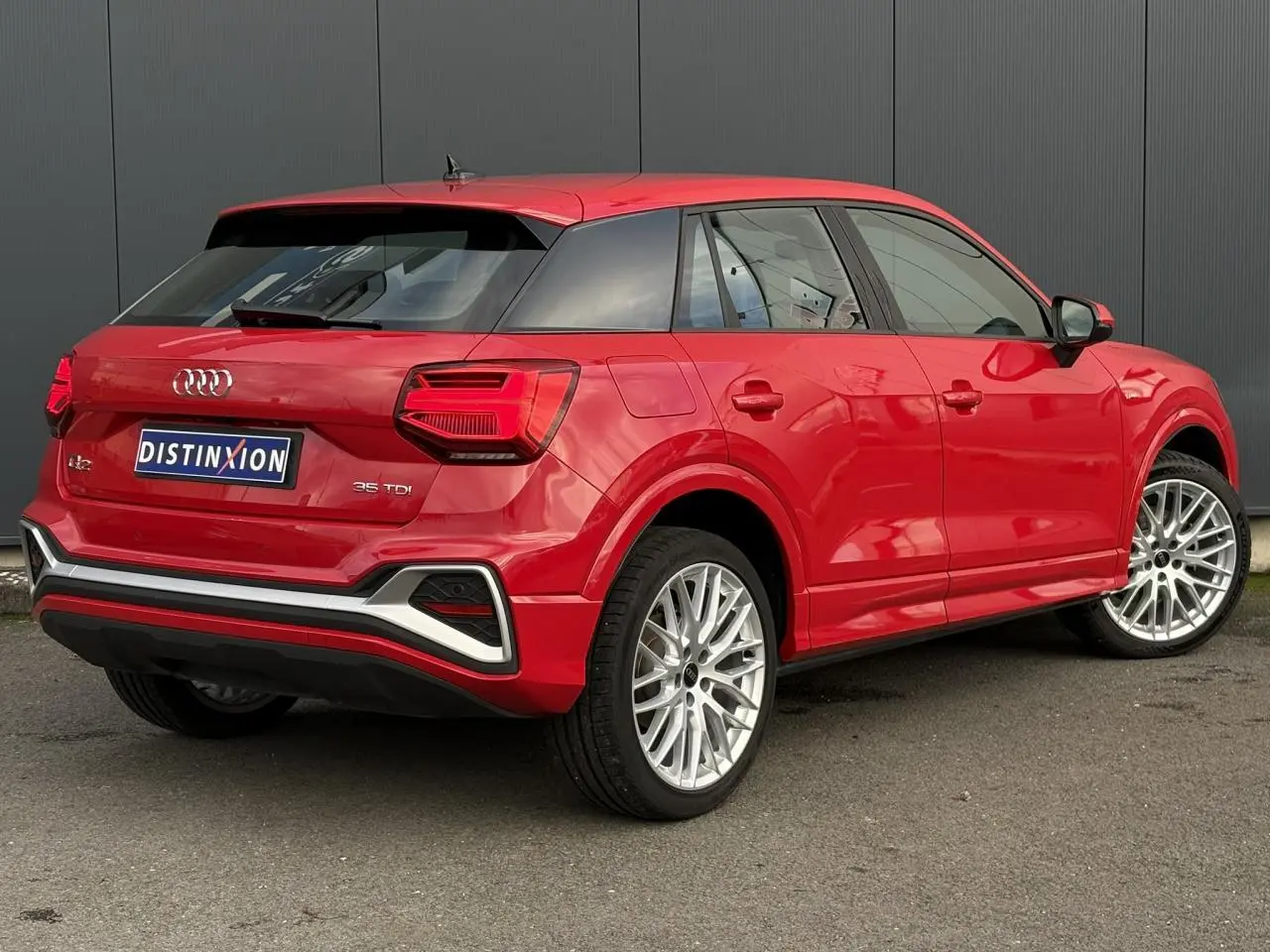 Audi Q2 35 TDI S-Line rouge vue 3/4 arrière droit, avec jantes alliage et feux arrière LED distinctifs.