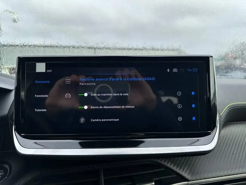 Écran tactile intérieur du Peugeot 2008 Hybrid 2025 affichant les aides à la conduite, avec détails de la planche de bord grise.