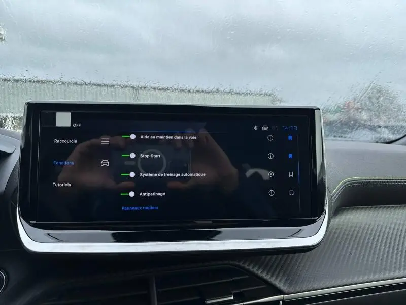 Écran tactile central du Peugeot 2008 gris 2025 affichant les aides à la conduite avec tableau de bord en arrière-plan.