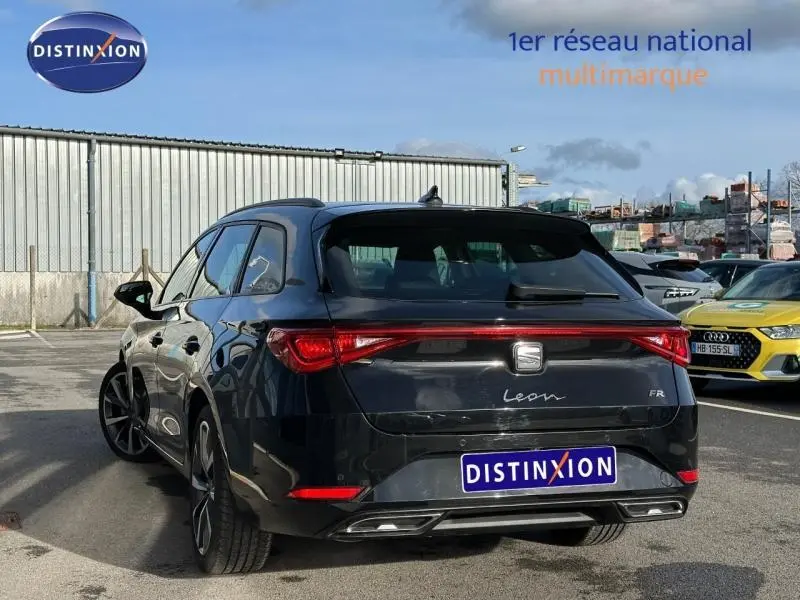 Vue 3/4 arrière d'une SEAT LEON ST 1.5 eTSI Hybrid noire métallisée avec feux arrière allongés et logo FR visible.
