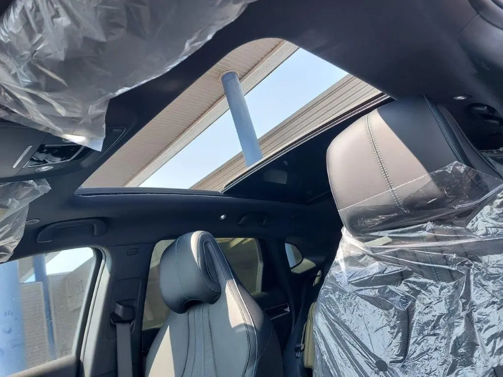 Vue intérieure du toit ouvrant panoramique et des sièges avant gris clair protégés par des housses plastiques sur BYD SEAL U DM-i BOOST 2026.