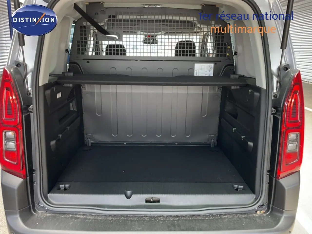 Coffre ouvert d’un Citroën Berlingo gris Artense métal, vue arrière montrant l’espace de chargement et la grille de séparation.