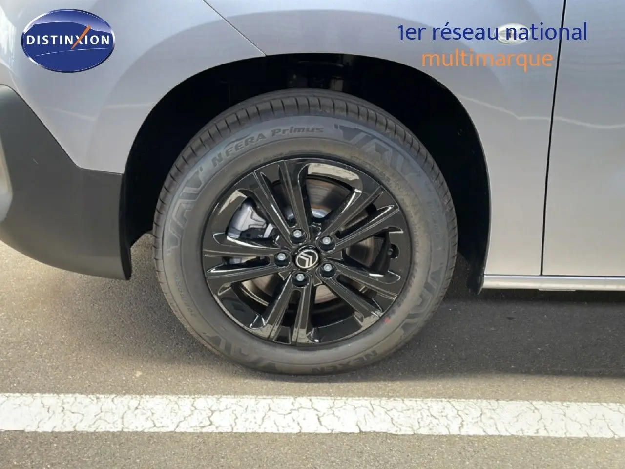 Gros plan sur la roue avant gauche noire brillante du Citroën Berlingo gris Artense métal, avec logo Citroën central.