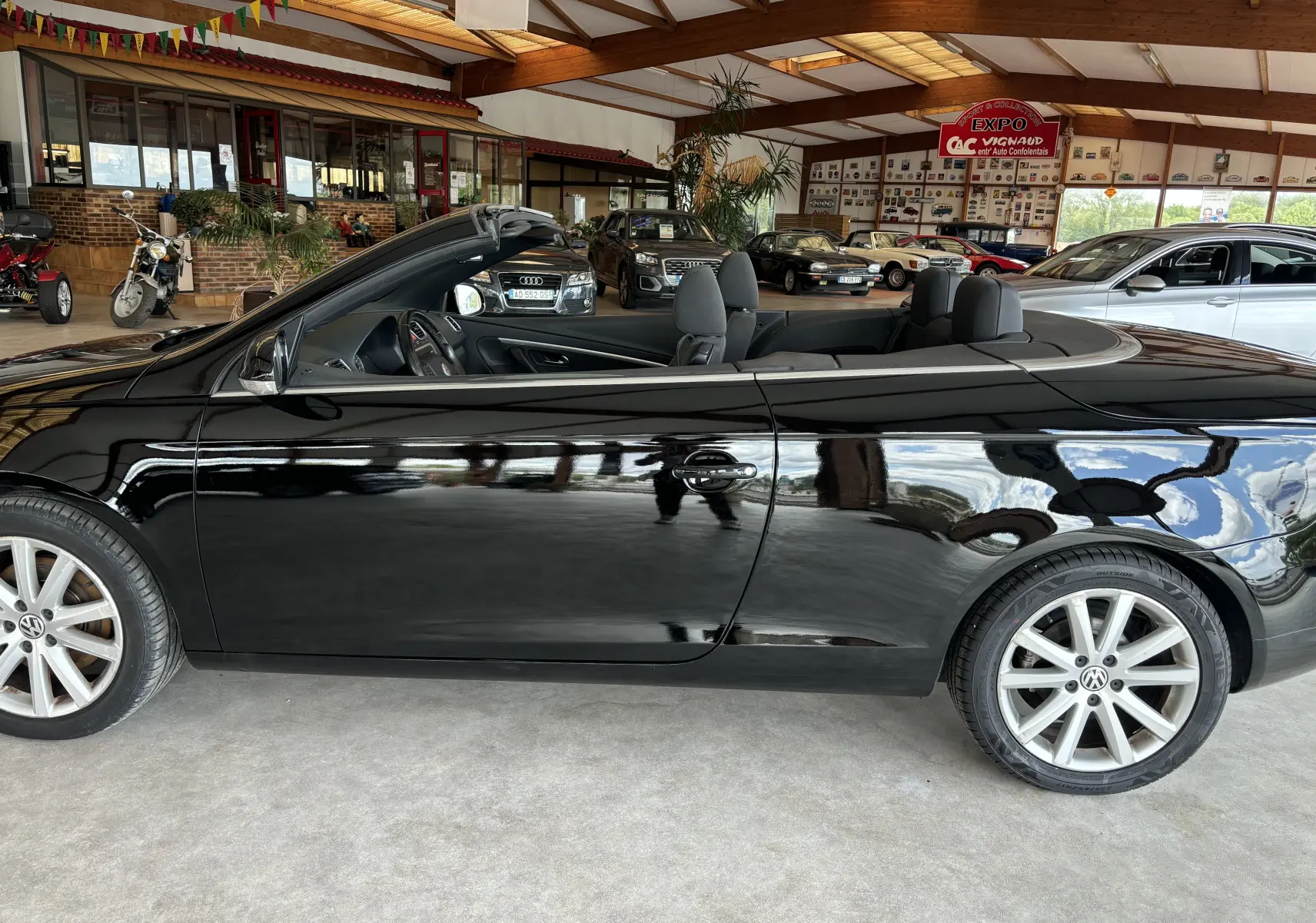 Volkswagen EOS cabriolet noir vue de profil côté gauche, intérieur visible, stationné en salle d'exposition.