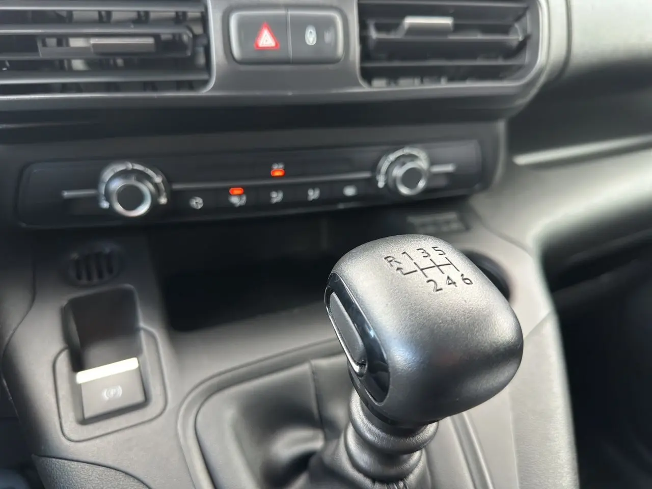 Gros plan sur le levier de vitesses manuel noir dans l'habitacle du Peugeot Partner blanc, avec commandes de climatisation visibles.
