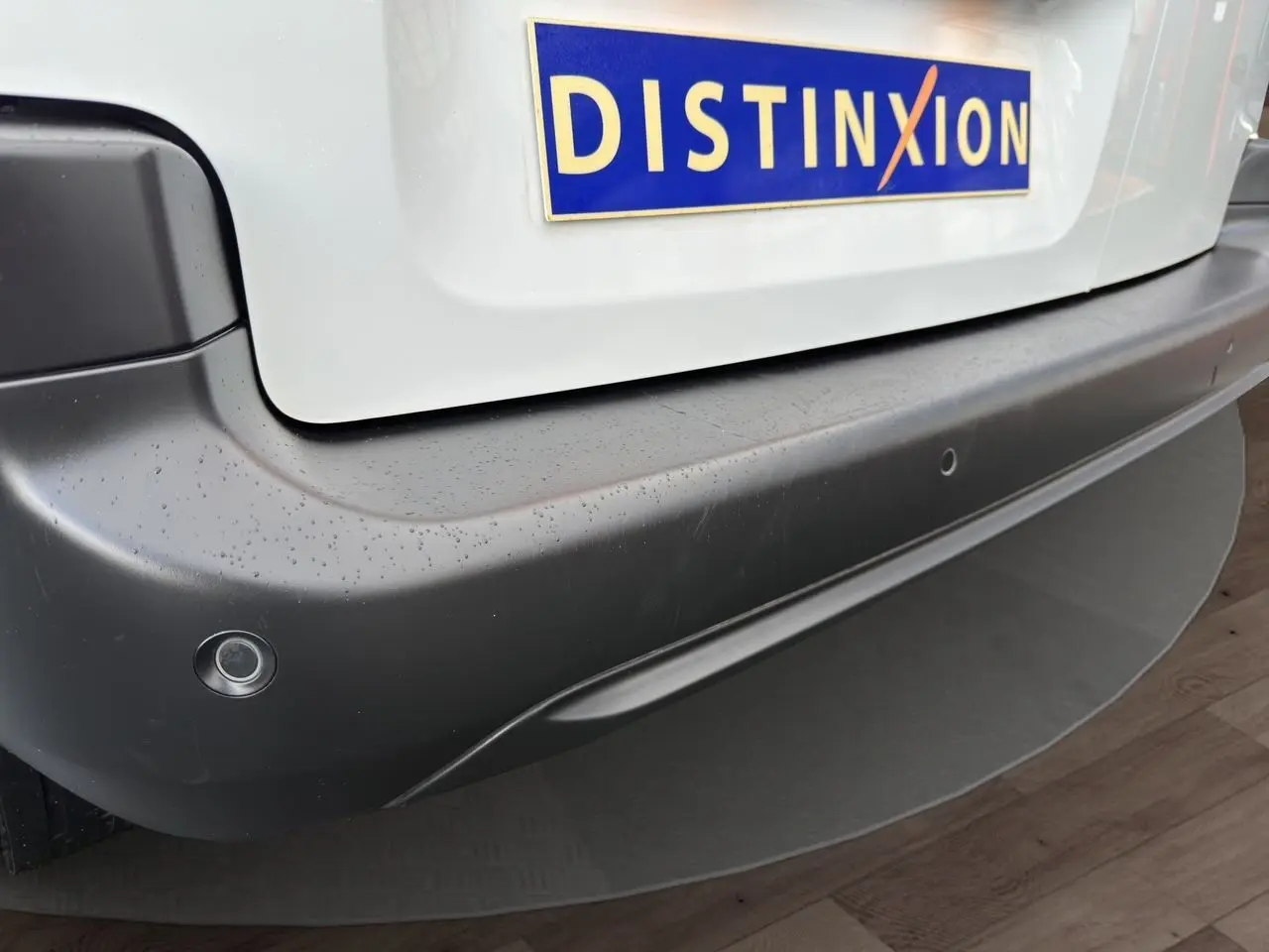 Gros plan sur le pare-chocs arrière noir d'un Peugeot Partner blanc avec capteurs de recul et plaque Distinxion.