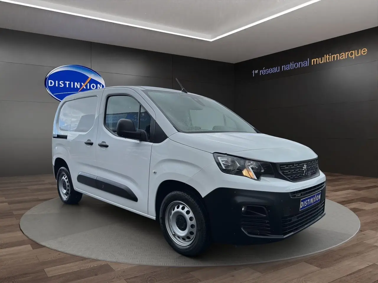 Vue 3/4 avant droite d'un Peugeot Partner blanc avec pare-chocs noir et jantes acier en showroom.