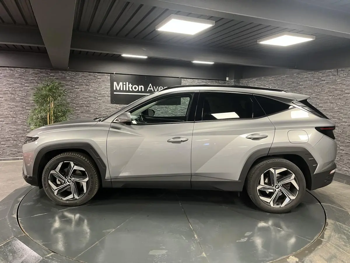 Profil côté gauche du Hyundai Tucson gris métallisé 2023 avec jantes alliage 19 pouces et toit noir contrasté.