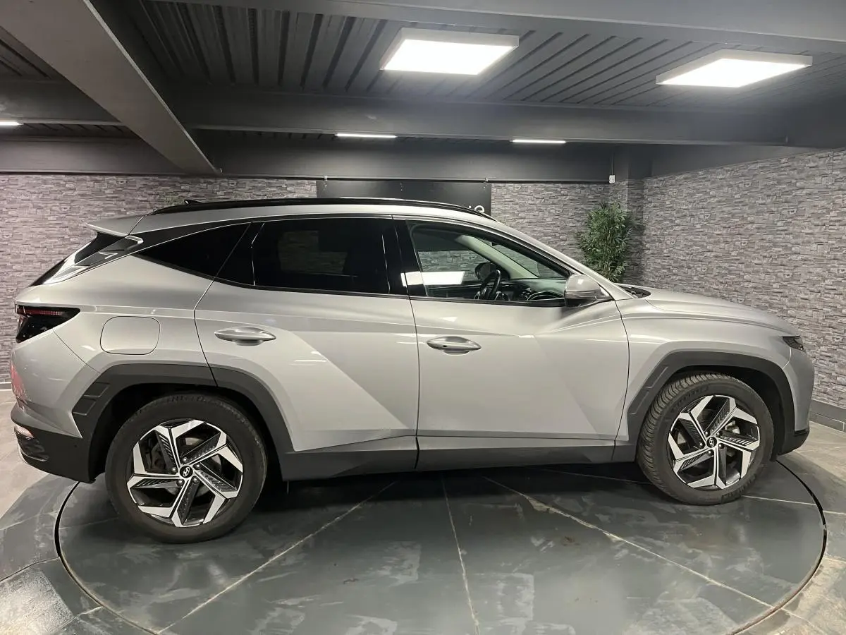 Profil côté gauche du Hyundai Tucson gris métallisé 2023 avec jantes alliage et lignes anguleuses marquées.